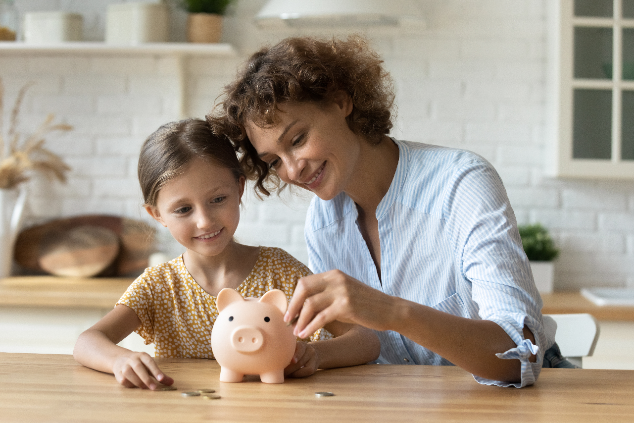 Kid and woman putting coins in a piggy bank